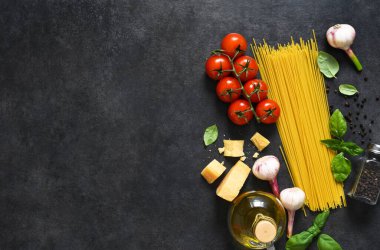 Makarna yapmak için gerekli malzemeler. Siyah arka planda domates ve fesleğenli çiğ spagetti. Yukarıdan görüntüle.