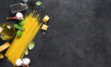 Makarna yapmak için gerekli malzemeler. Siyah arka planda fesleğenli çiğ spagetti. Yukarıdan görüntüle.