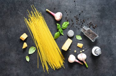 Makarna yapmak için gerekli malzemeler. Siyah arka planda fesleğenli çiğ spagetti. Yukarıdan görüntüle.