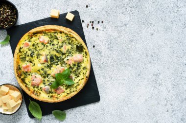 Beton zeminde taş bir tahtada somon, ıspanak ve peynirli turta (quiche). Yukarıdan görüntüle.