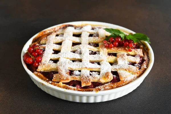 Cherry pie sprinkled with icing sugar on a wooden, brown background.