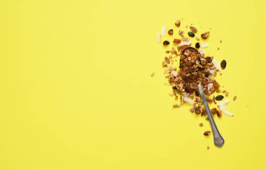 Sarı arka planda kaşıkta fındıklı granola. Üst görünüm.