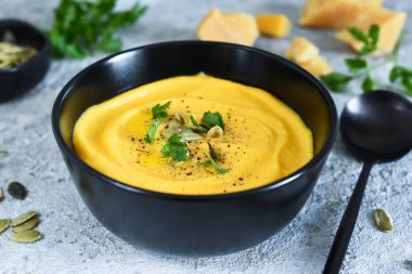 Balkabağı püresi çorbası kremalı ve balkabağı tohumlu beton arka planda.