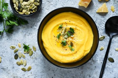 Balkabağı püresi çorbası kremalı ve balkabağı tohumlu beton arka planda.