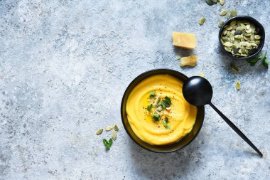 Balkabağı püresi çorbası kremalı ve balkabağı tohumlu beton arka planda.