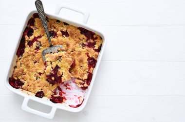 Kirazlı ev yapımı yaz tatlısı. Beyaz bir zemin üzerinde kirazlarla bir fırın kabında ezilmek.