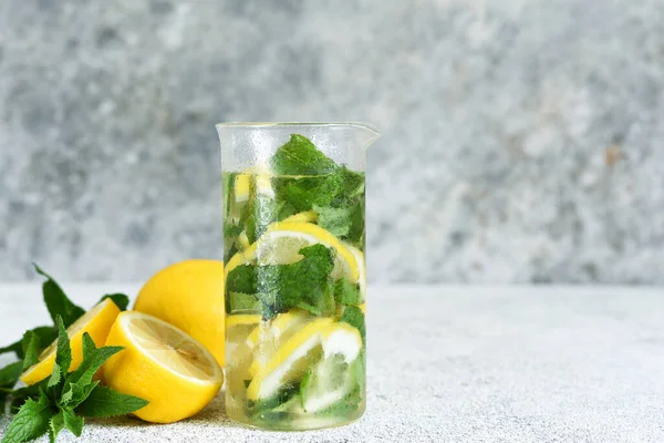 Lemonade with syrup and mint in a glass cup on a concrete background.
