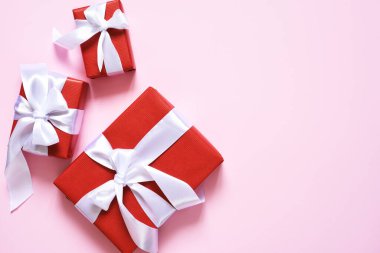 Pembe arka planda beyaz kurdeleli bir sürü kırmızı kutu. Hediyelerle dolu kutular. Yukarıdan bak. Düzgünce