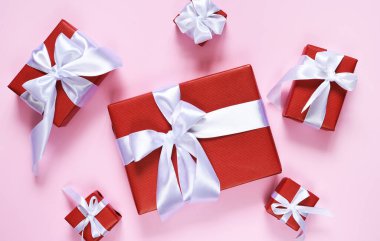 Pembe arka planda beyaz kurdeleli bir sürü kırmızı kutu. Hediyelerle dolu kutular. Yukarıdan bak. Düzgünce