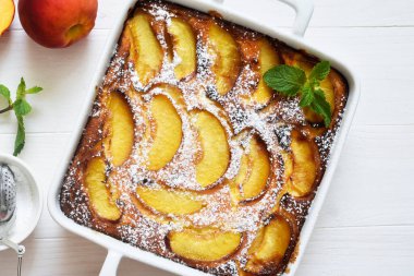 Şeftalili pasta, beyaz ahşap arka planda pudra şekeri serpiştirilmiş.