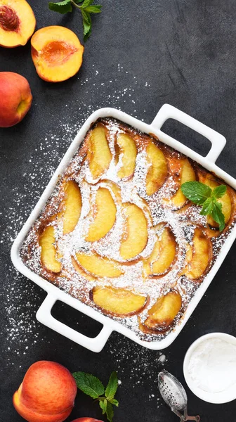 Delicate cake with peaches sprinkled with powdered sugar on a black concrete background