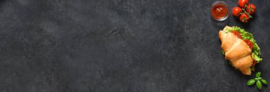 Baner. Kruvasan sandviçli kahvaltı, salata yapraklı, jambonlu ve vişneli domatesli, siyah arka planda sos. Yukarıdan görüntüle.