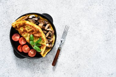 Kahvaltı için mantarlı omlet ve domatesli turuncu çubuklu beyaz beton arka planda..