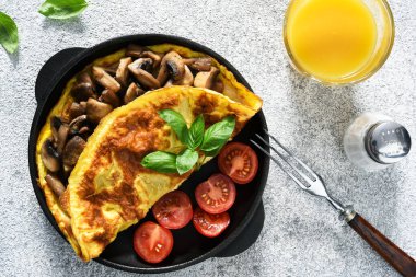 Kahvaltı için mantarlı omlet ve domatesli turuncu çubuklu beyaz beton arka planda..
