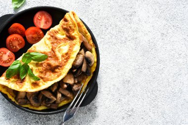Kahvaltı için mantarlı omlet ve domatesli turuncu çubuklu beyaz beton arka planda..