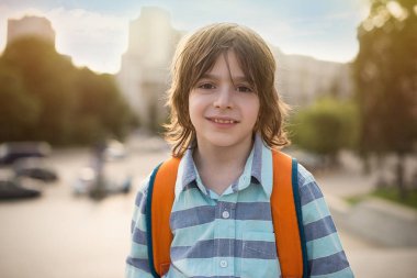 Onun omuzlarında bir el çantası ile gülümseyen bir okul çocuğu duygusal portresi. Büyük bir şehir meydanında standları, yüksek binalar uzaktan görülebilir.