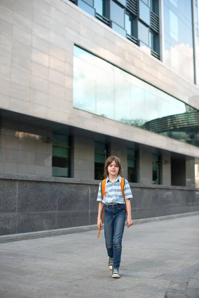 Liseli sarışın bir gömlek ve pantolon giyen bir sırt çantası ile büyük bir kaldırım kare okula gider.