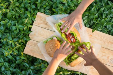 Ahşap kurullarında dokusal parşömen peçete bir bahçe piknik üzerinde yatan hamburger için ulaşmak için üç çocuk eller.