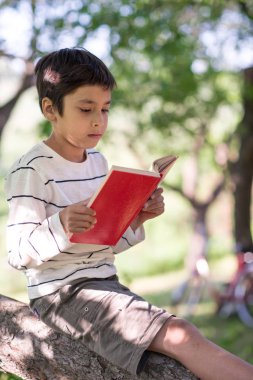 Bir okul çocuğu kitap ve okuma ağacıyla oturur.  