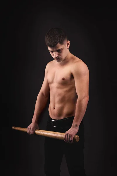View of a muscled man   with  baseball bat on a black background in studio