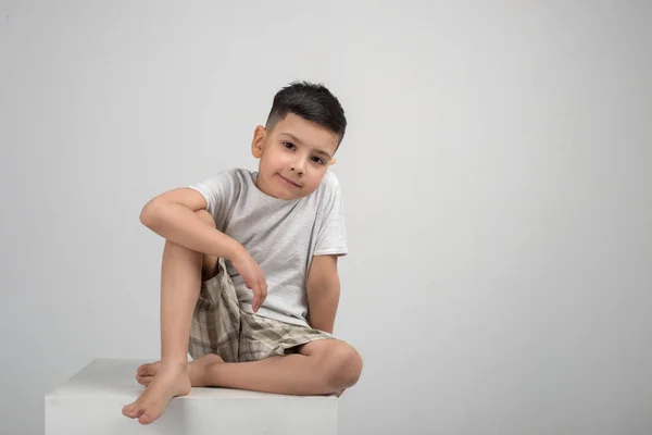 Niño Sonriente Morena Con Camisa Gris Sienta Sobre Pedestal Blanco —  Fotos de Stock