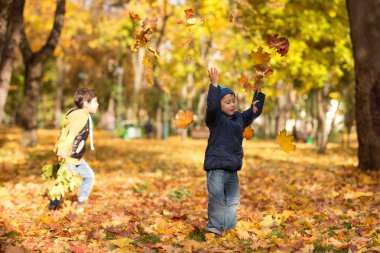 İki erkek sonbahar parkta yürüyorlar. Sevinçle kot pantolon ve mavi bir ceket giymiş küçük bir çocuk sarı yapraklar yukarı atar. 