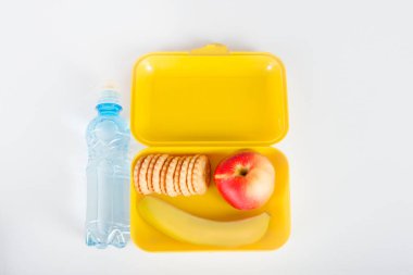  Öğle yemeği ile sarı plastik kutu ve okul için su şişesiyle yalan beyaz bir masaya. Bir muz, elma ve bisküvi kutusuna vardır, 