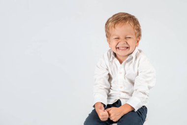 Yarım uzunlukta duygu beyaz gömlek giymiş küçük bir gülen çocuk portresi. O stüdyoda beyaz bir arka plan üzerinde siting