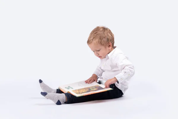 Beyaz gömlek ve blask pantolon giyen biraz ciddi boyl tam uzunlukta portresi. O profilde katta oturan ve bir çocuk kitabı stüdyoda beyaz bir arka plan üzerinde düşünüyor.