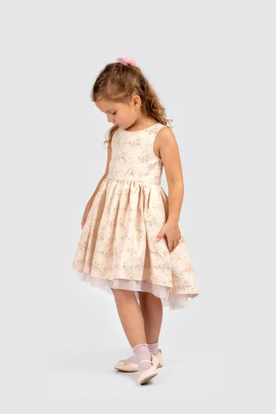 一个面带微笑的小女孩穿着美丽的米色优雅礼服的全长肖像 她站在演播室的白色背景上 — 图库照片