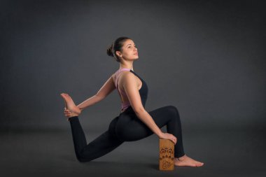 Germe Egzersiz Studio, tam uzunlukta gri arka plan üzerinde bir tuğla kullanarak siyah spor giyim giymiş esmer genç sakin güzel kadın yok.  