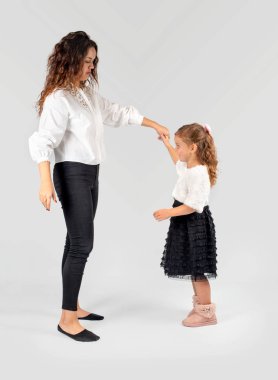 Tam uzunlukta genç kadın - anne ya da öğretmen ve güzel siyah zarif elbise giyen bir gülümseyen kız portresi. Kadın kıza beyaz bir arka planda stüdyoda dans etme öğretir