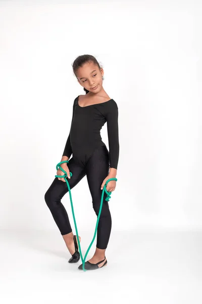 Studio shot of   attractive little  gymnast girl of mulatto wearing  black leggings and a bathing suit with a green jump rope on a white background, full length.