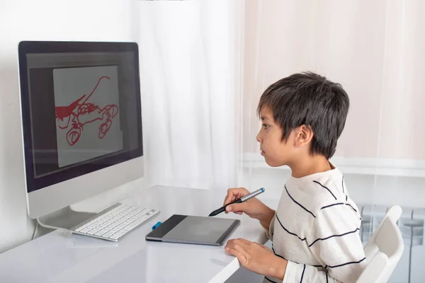 Schoolboy enthusiastically draw on a computer using a tablet in the room