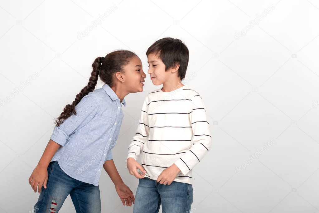 Studio shot of   attractive little girl and boy wearing shirts and jeans on a white background. A girl whispers to the boy something .  They are having fun.
