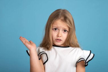 Duygusal portre Studio mavi zemin üzerine beyaz blous siyah şeritler ile giyen genç sarışın kız kapatın. O uzakta belgili tanımlık palmiye gösterir ve bir şey hakkında şikayet ya da bir şey ile memnuniyetsizliği ifade eder.