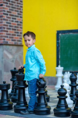 Küçük bir seriouse çocuk giyiyor mavi tişört ve kot çalış ile satranç oyun