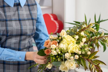 Bir çiçekçi bir buket gül yapma stüdyo çekim. Yakınlarda bir kırmızı hediye şeklinde bir kalp kutun.