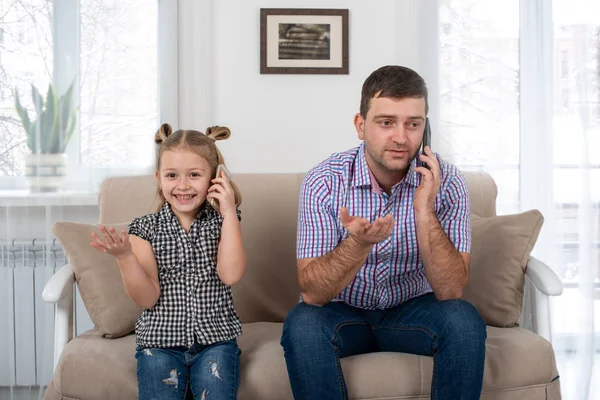 演播室拍摄了一个女儿和爸爸坐在家里的沙发上 用同样的方式打电话 女儿模仿她的父亲 — 图库照片
