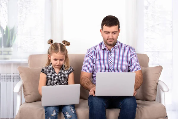 演播室拍摄的女孩坐在沙发上与爸爸在家里与笔记本电脑 女儿模仿爸爸 — 图库照片