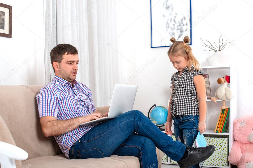 A girl with a textbook in her hands went to her dad and asked him to help with the lessons.  Dad is sitting on the couch with a laptop, he is very busy.  The daughter is ignored by the father, she is upset 