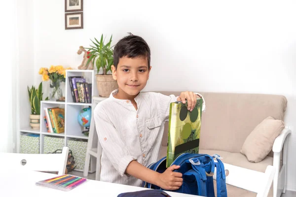 Улыбающийся школьник собирает портфель в школе, добавляет фол — стоковое фото