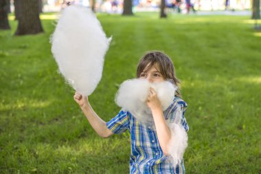 Papyonlu mavi gömlek giyen bir çocuk pamuk şeker yiyor
