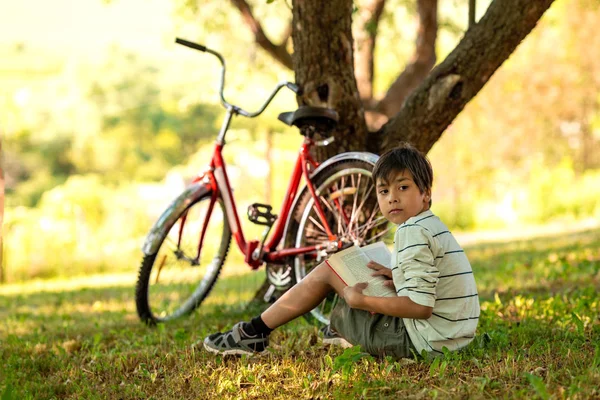 Pojken sitter på gräset i trädgården och tänker på boo — Stockfoto