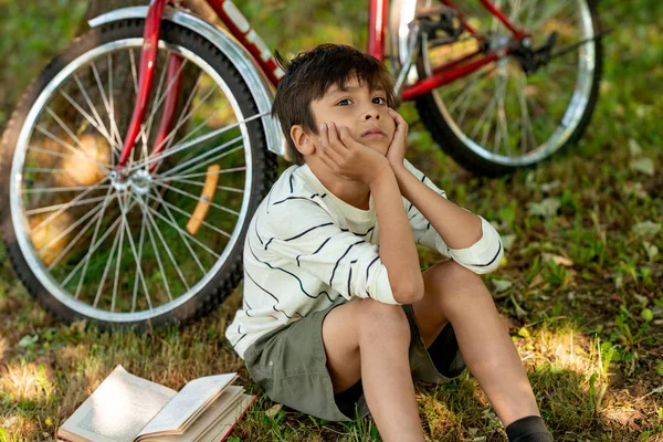 Pojken sitter på gräset i trädgården och tänker på boo — Stockfoto