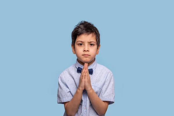 Niño serio rezar contra el fondo azul con espacio de copia . — Foto de Stock