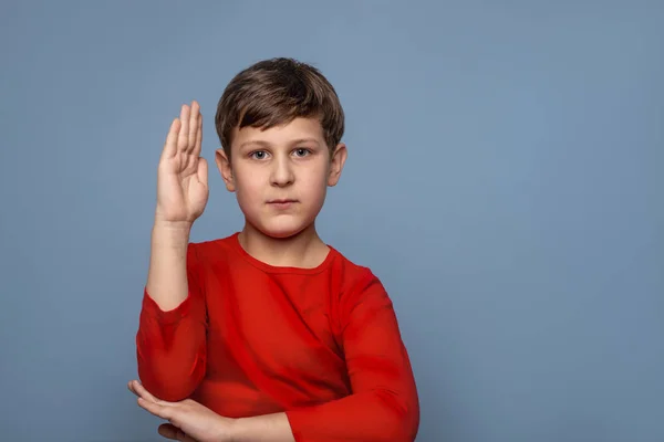 Een serieuze school jongen dragen rode shirt verhoogd zijn hand tot ans — Stockfoto