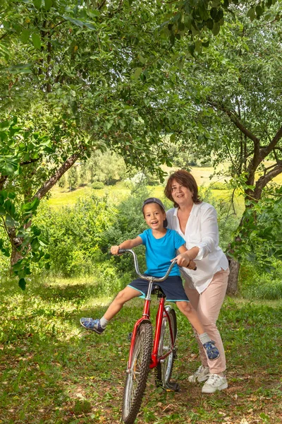 Бабушка едет на большом красном велосипеде внука в гарде — стоковое фото