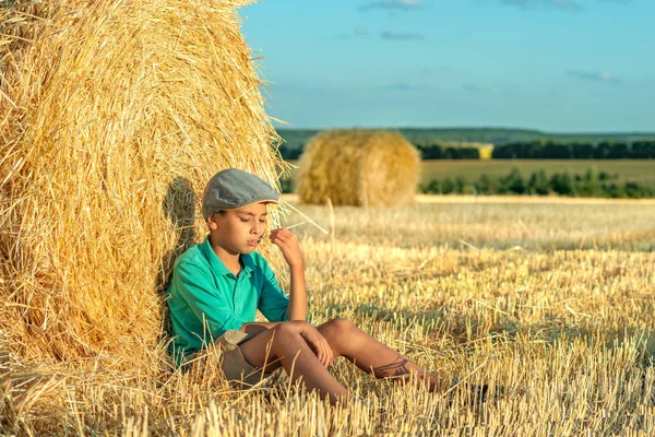 Ein Junge sitzt an einem sonnigen Tag an einem Heuhaufen auf einem Feld und ich denke, — Stockfoto