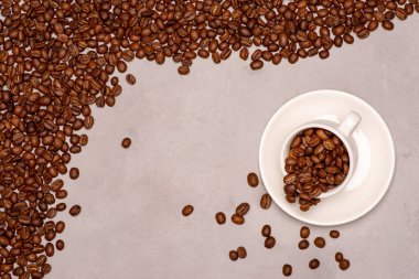 Kahve taneleri gri dokulu bir yüzeye serpilir. Yakınlarda ters çevrilmiş bir fincan kahve çekirdeği vardır. Kopya alanı. Neşe ve iyi ruh hali kavramı.